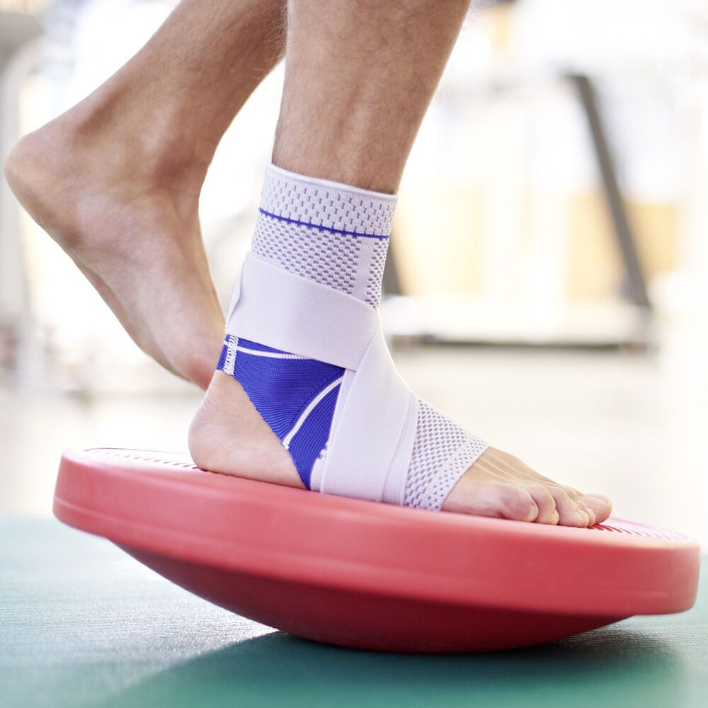 Person mit MalleoTrain S open heel auf einem Balance-Board. Der Knöchel ist mit der Bandage geschützt.