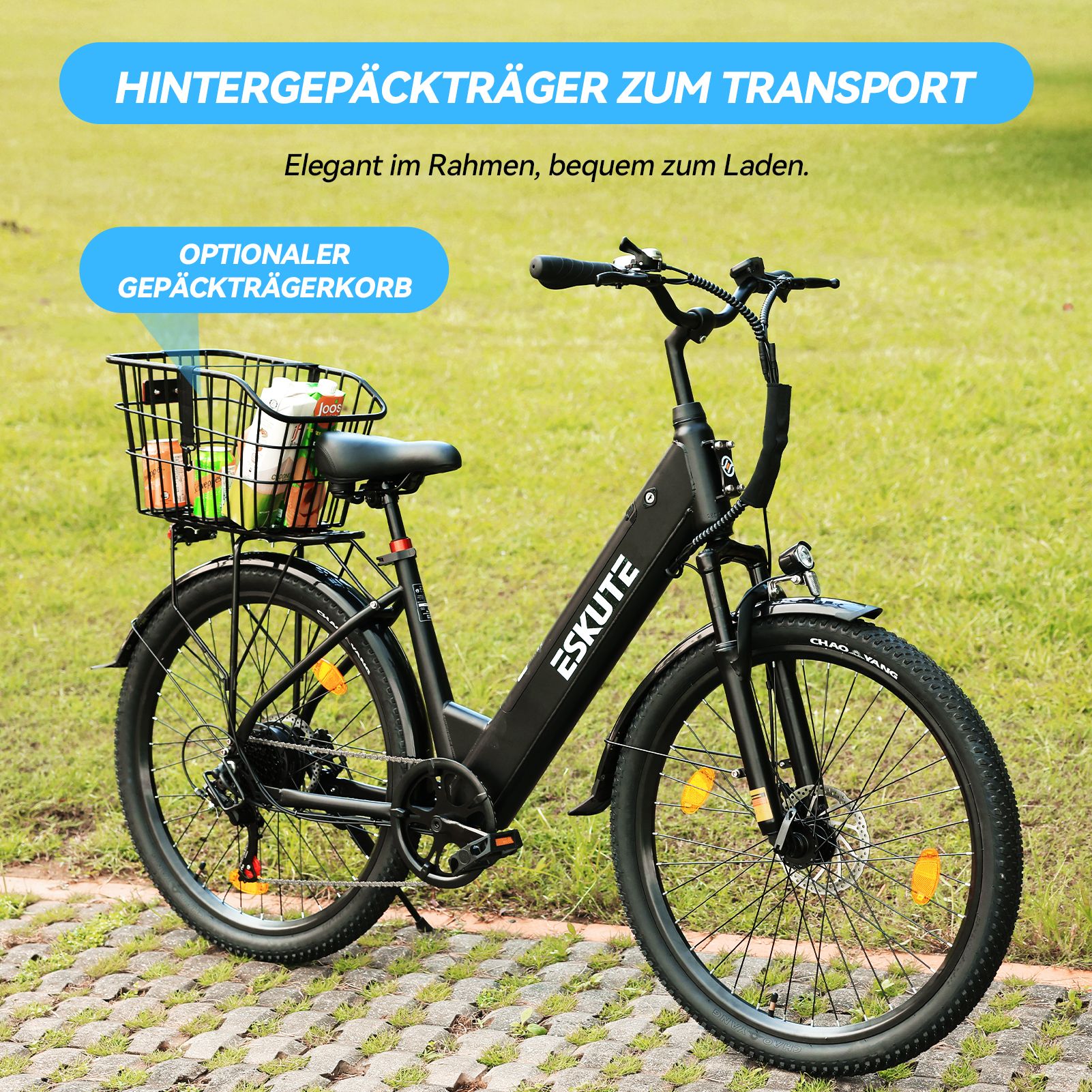 Schwarzes ESKUTE Elektro-Citybike mit Gepäckträgerkorb. Der Korb enthält Gegenstände. Das Fahrrad steht auf einer grünen Wiese.