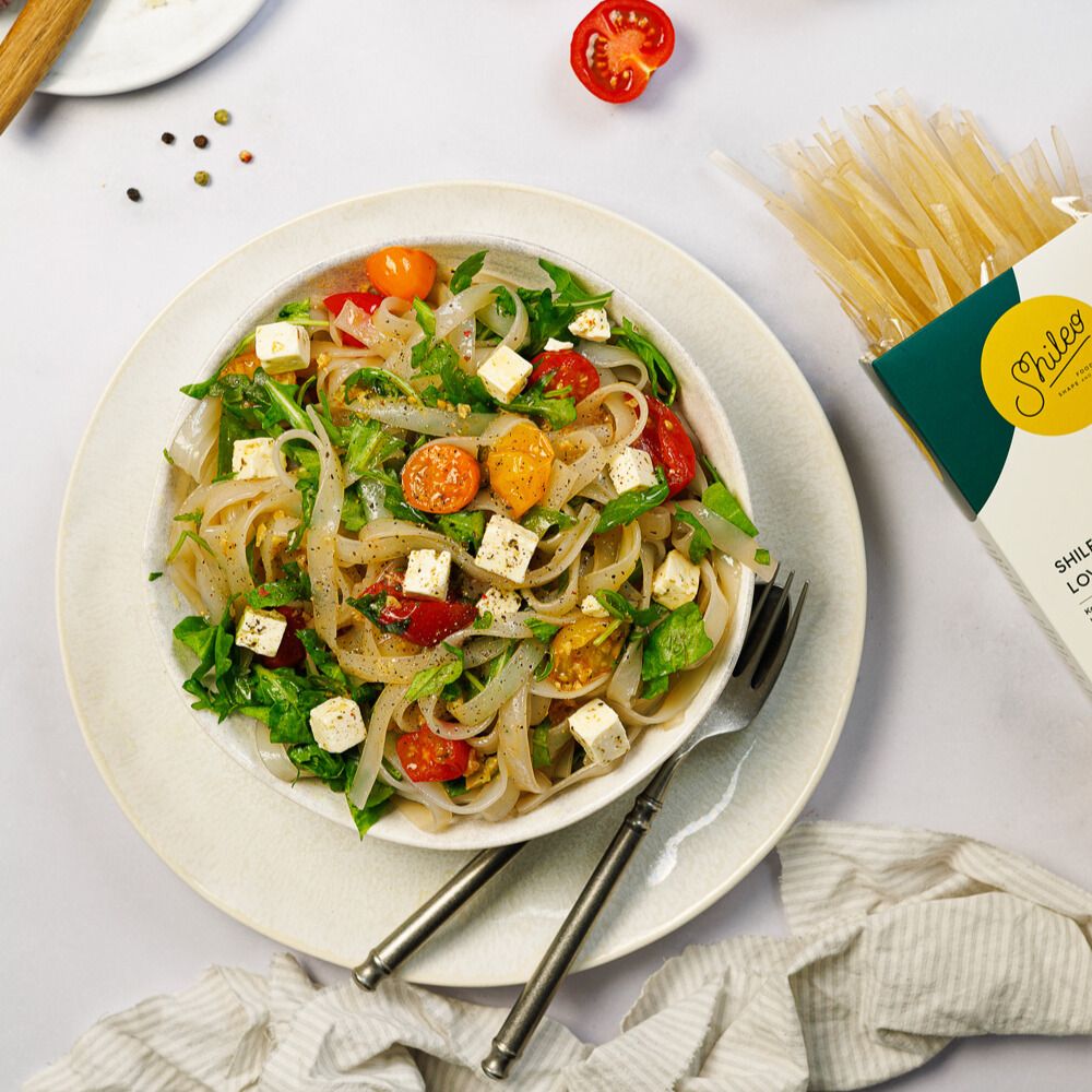 Teller mit Salat und Nudeln. SHILEO Lower-Carb Fettuccine Packung rechts. Tomaten, Käse und Kräuter.