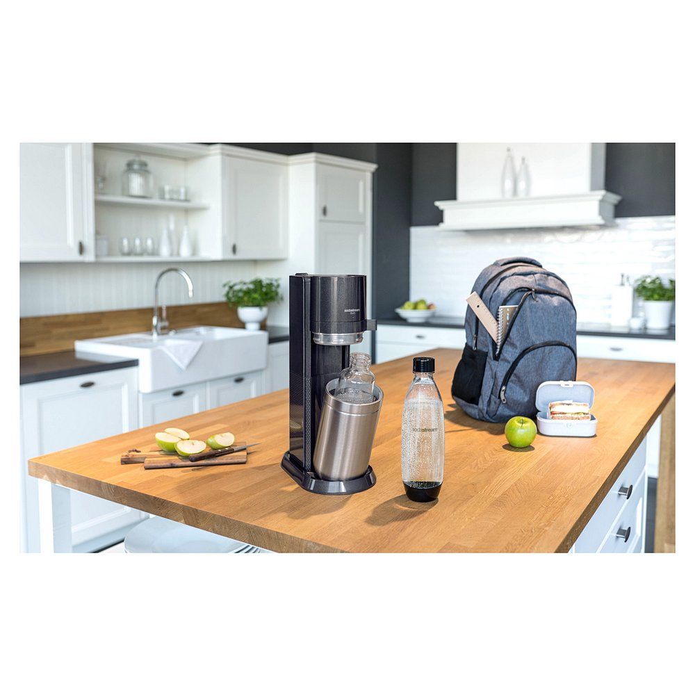 SodaStream Duo in einer Küche auf einer Holzoberfläche, neben einer Flasche und einem Rucksack.