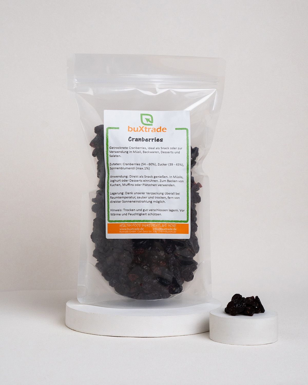 Beutel mit Cranberries auf weißem Podest. Etikett mit Produktinformationen. Kleine Menge Cranberries daneben.