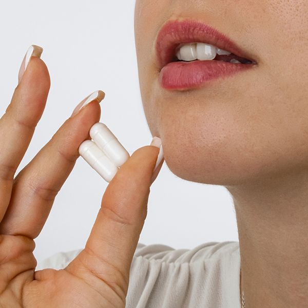 Eine Frau hält zwei weiße Kapseln zwischen Daumen und Zeigefinger.