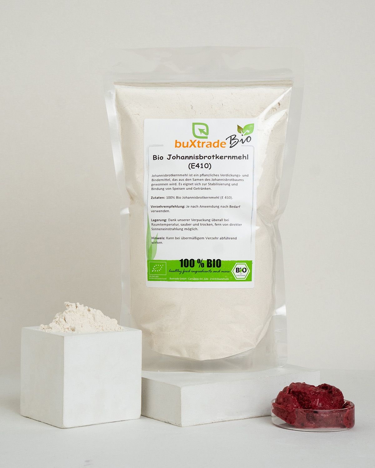 Verpackung mit Johannisbrotkernmehl, daneben ein Würfel mit Mehl und eine Schale mit Beeren.