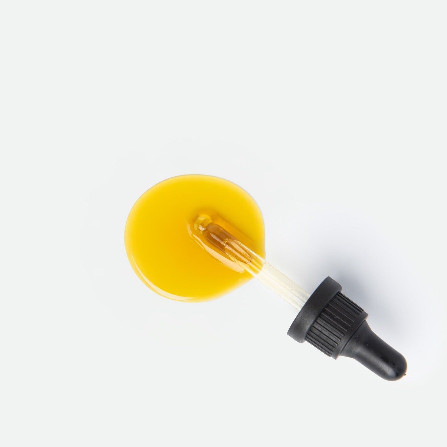 Gelber Öl-Tropfen mit Glas-Pipette und schwarzem Tropfer auf weißem Hintergrund.