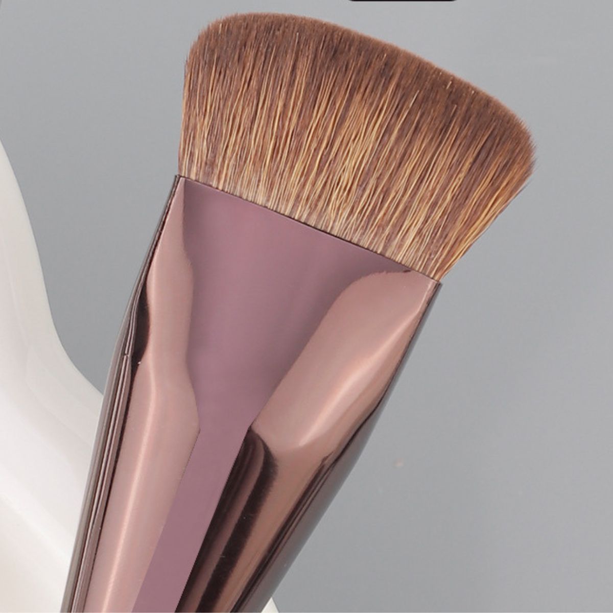 Abgewinkelte flache Make-up-Pinsel mit roségoldfarbenem Griff und dichten, braunen Borsten.