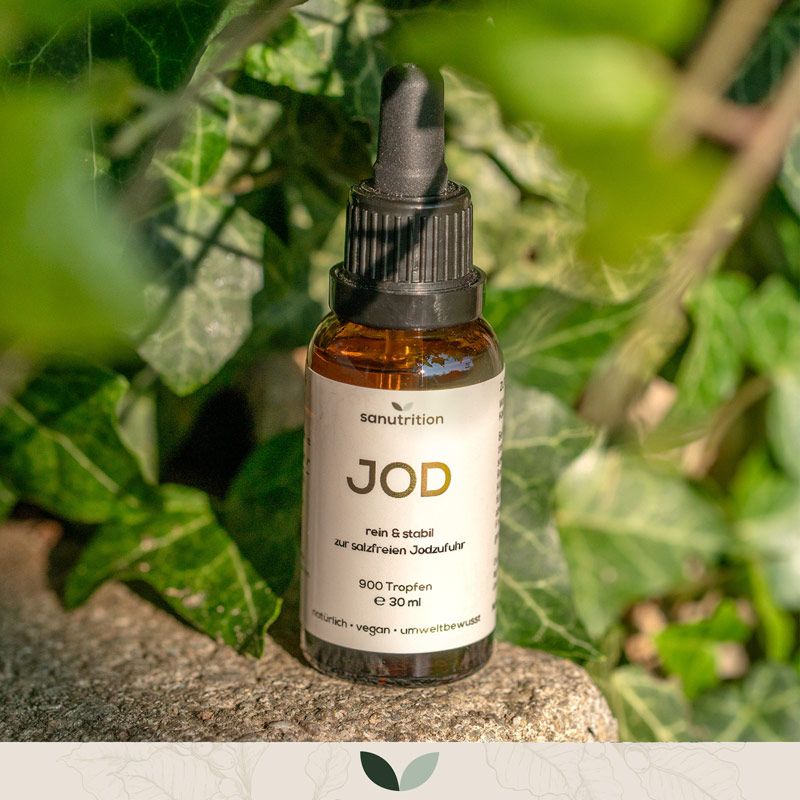 Braune Glasflasche mit schwarzem Tropfer. Etikett mit "JOD", "900 Tropfen", "vegan". Im Grünen platziert.