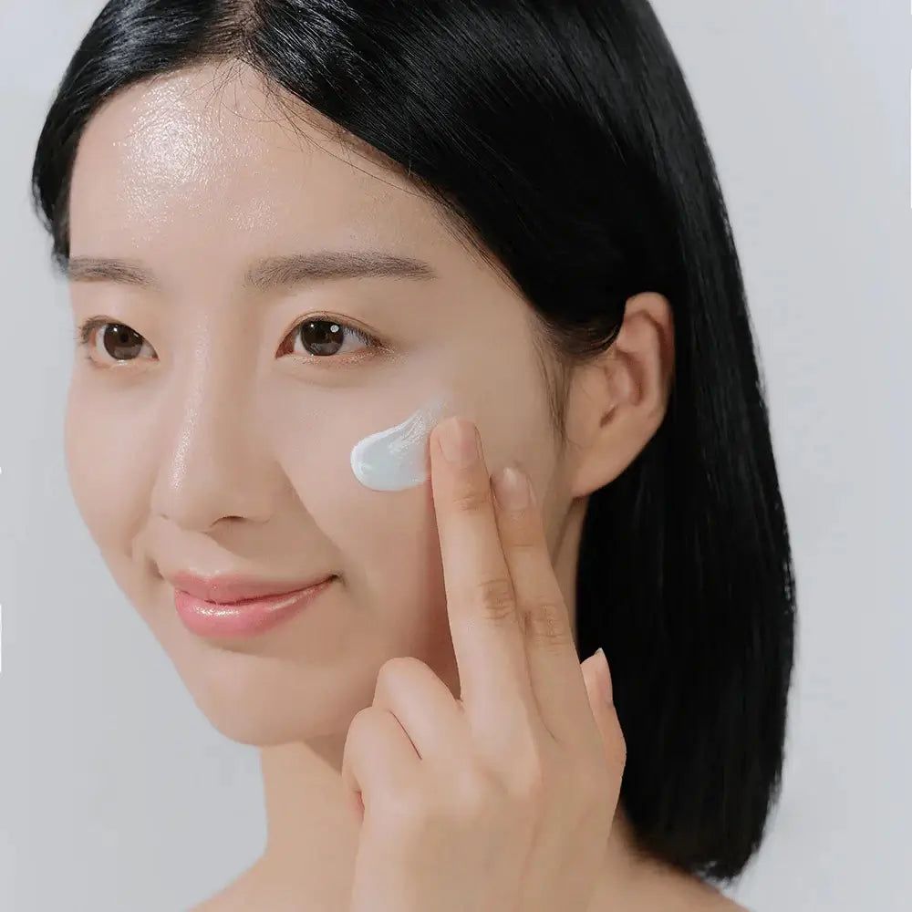 Frau trägt Creme auf Gesicht auf. Helle Creme auf der Haut. Helle Haut. Schwarze Haare.