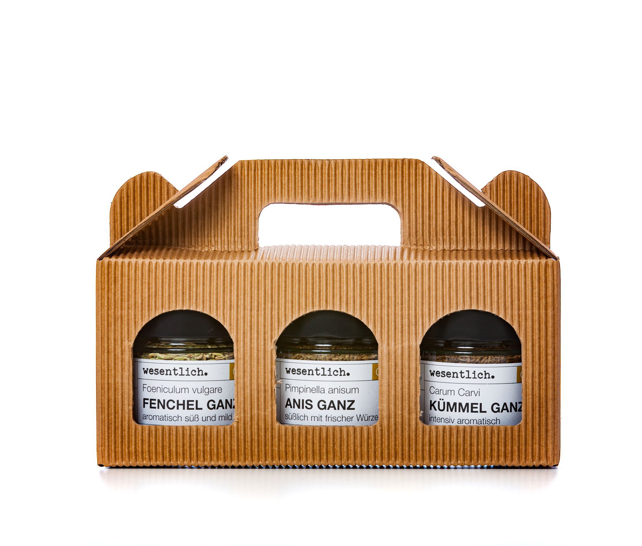 Tragetasche aus Pappe mit drei Gewürzgläsern. Sichtbare Etiketten: Anis, Fenchel, Kümmel. Marke: wesentlich.