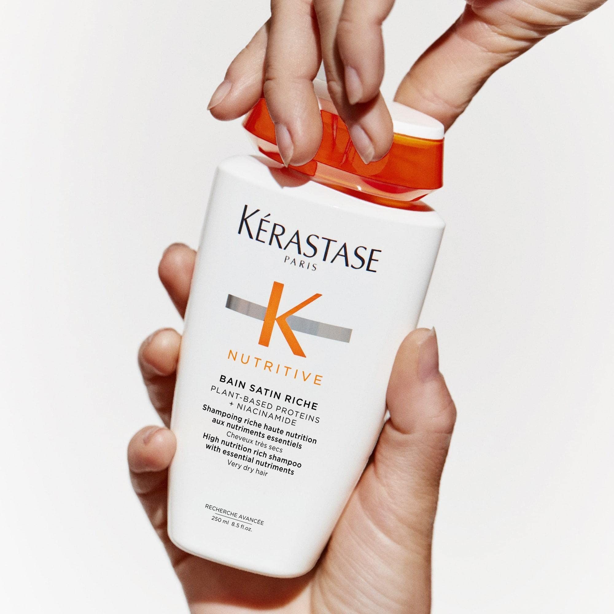 Hände öffnen eine Kérastase Nutritive Bain Satin Riche Shampoo-Flasche.