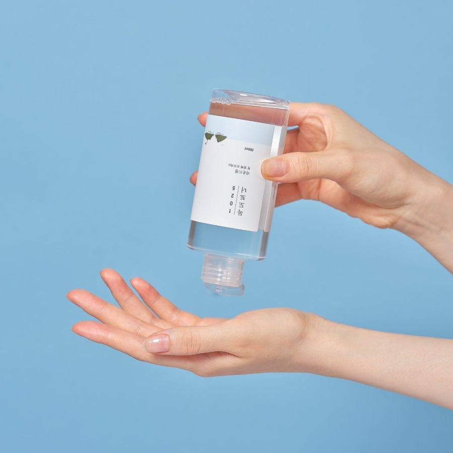 Transparente Flasche mit weißem Etikett. Hände halten die Flasche über einer Handfläche. Blauer Hintergrund.