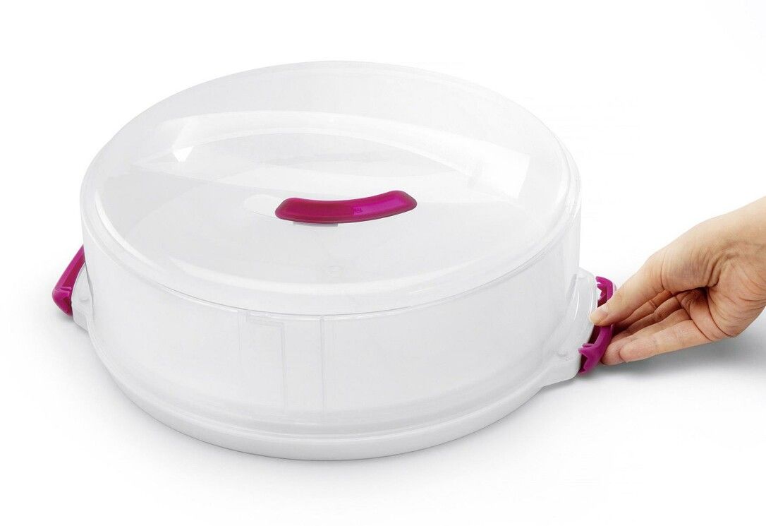 Weißer, runder Kuchenbehälter mit transparentem Deckel und pinkfarbenen Griffen. Hand öffnet einen Verschluss.