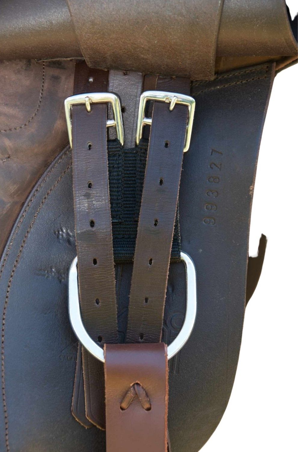 Braune Lederriemen mit silbernen Schnallen und D-Ring, an einem Sattel befestigt. Schwarzer Textilriemen.