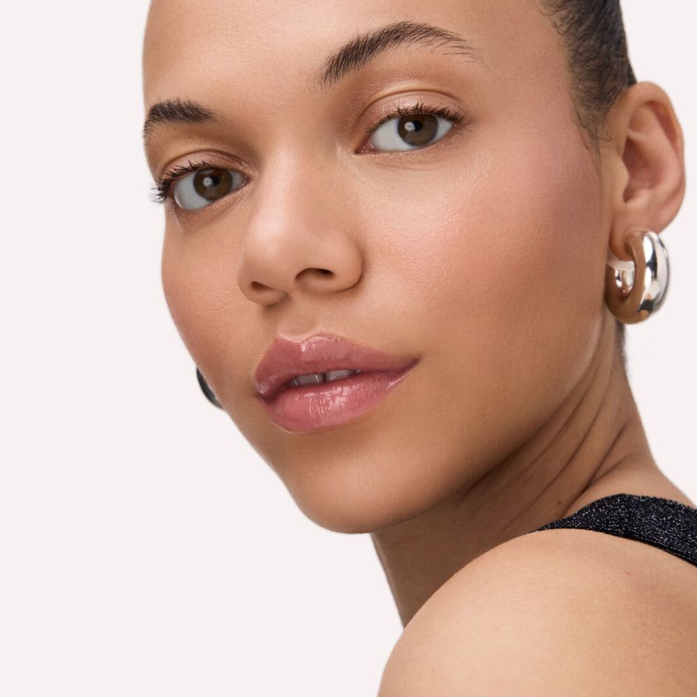 Porträt einer Frau mit glänzendem Lipgloss auf den Lippen. Sie trägt Creolen.