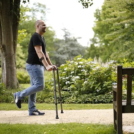 Mann geht mit zwei Unterarmgehhilfen im Park. Die Gehhilfen sind am Arm befestigt.