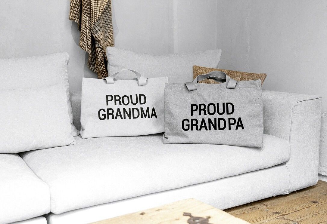 Zwei Leinwandtaschen auf einem Sofa. Eine mit "PROUD GRANDPA", die andere mit "PROUD GRANDMA".
