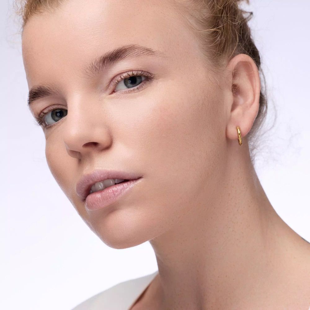 Porträt einer Frau mit hellem Teint. Sie trägt goldene Ohrringe.