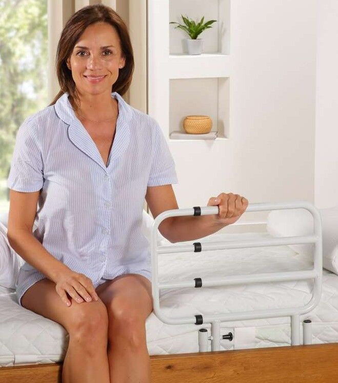 Frau sitzt auf einem Bett und hält ein weißes, ausziehbares Bettgeländer. Sie trägt Schlafanzug.