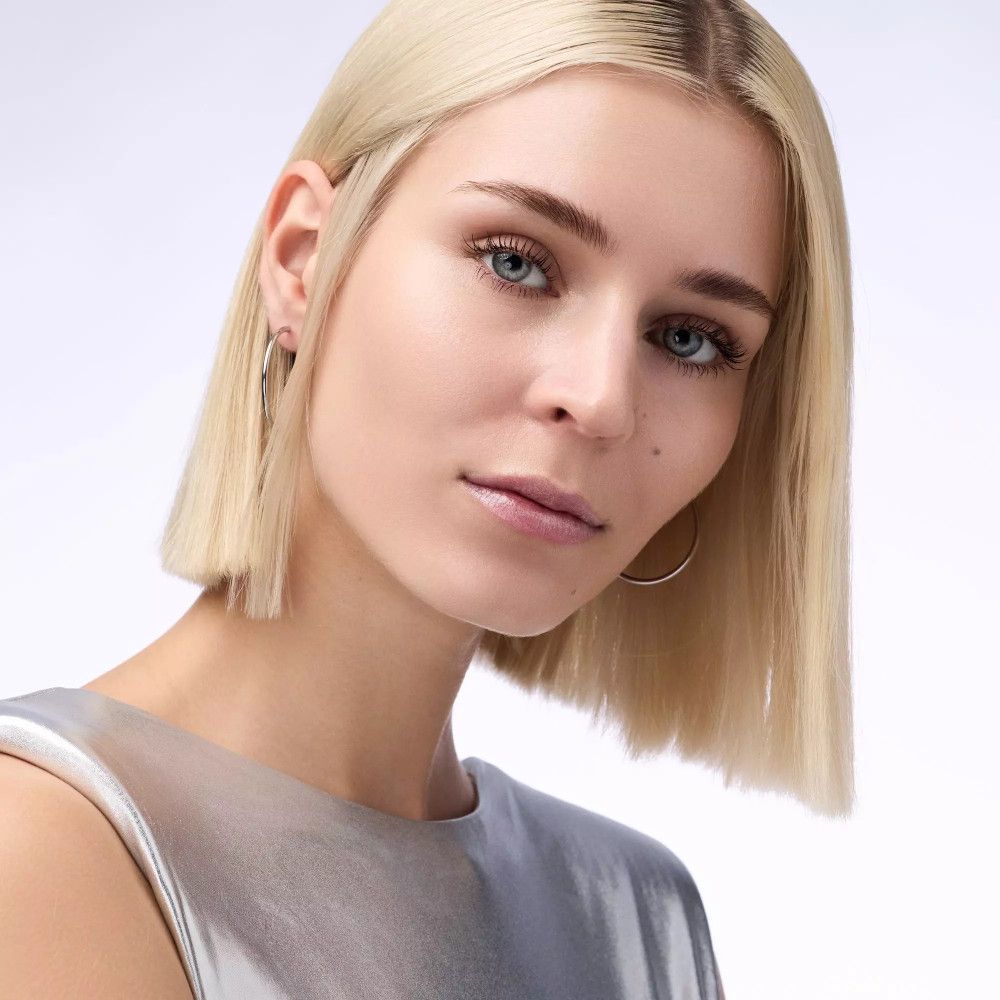 Porträt einer Frau mit blonden Haaren und blauen Augen. Sie trägt Ohrringe.