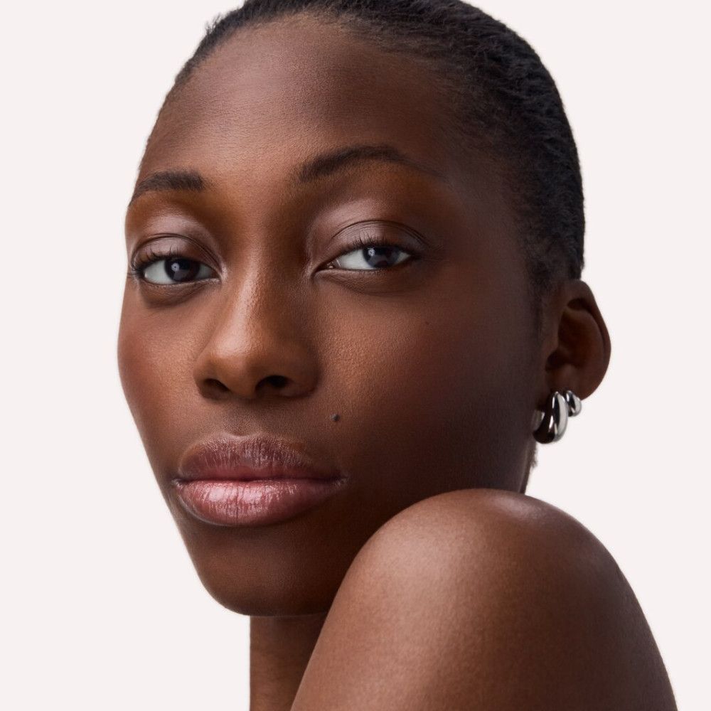 Porträt einer Frau mit dunkler Haut. Sie trägt silberne Creolen. Die Lippen sind mit Lip Balm betont.