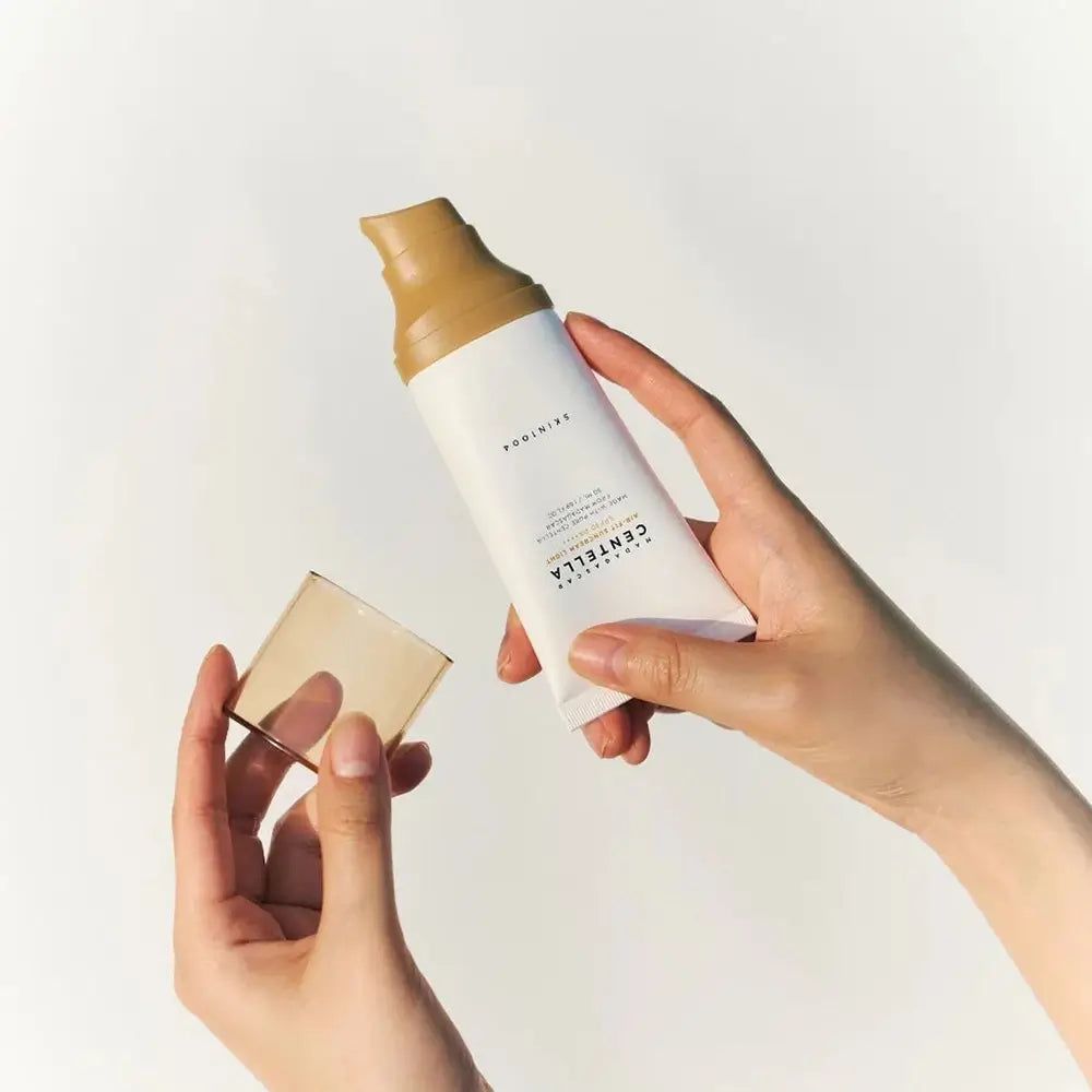 Weiße Tube mit braunem Deckel, gehalten von Händen. Aufschrift: CENTELLA. Produktname nicht vollständig sichtbar.