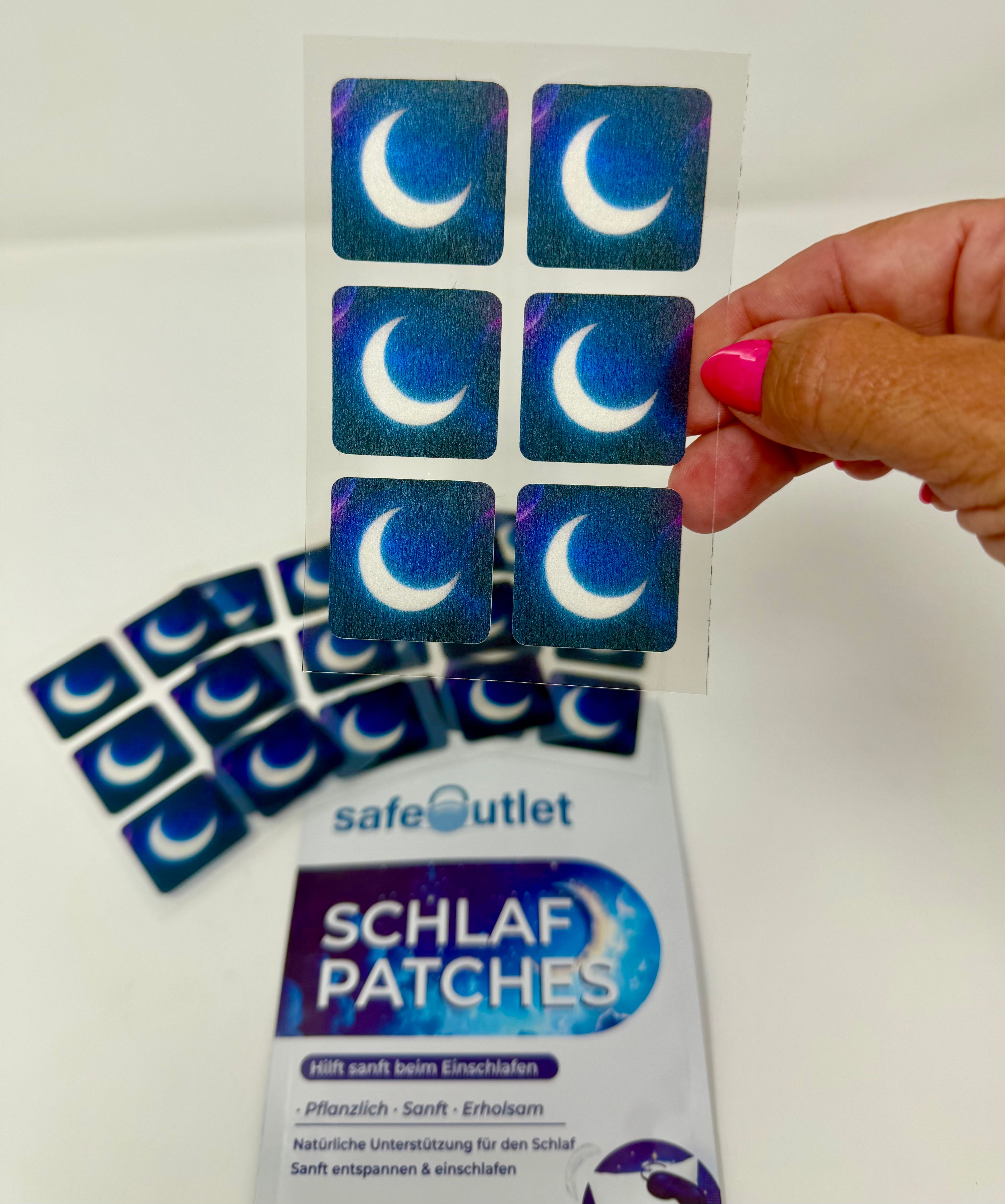 Ein Blatt mit sechs Schlaf-Patches mit Mondmotiv, das von einer Hand gehalten wird. Darunter liegt eine Packung.