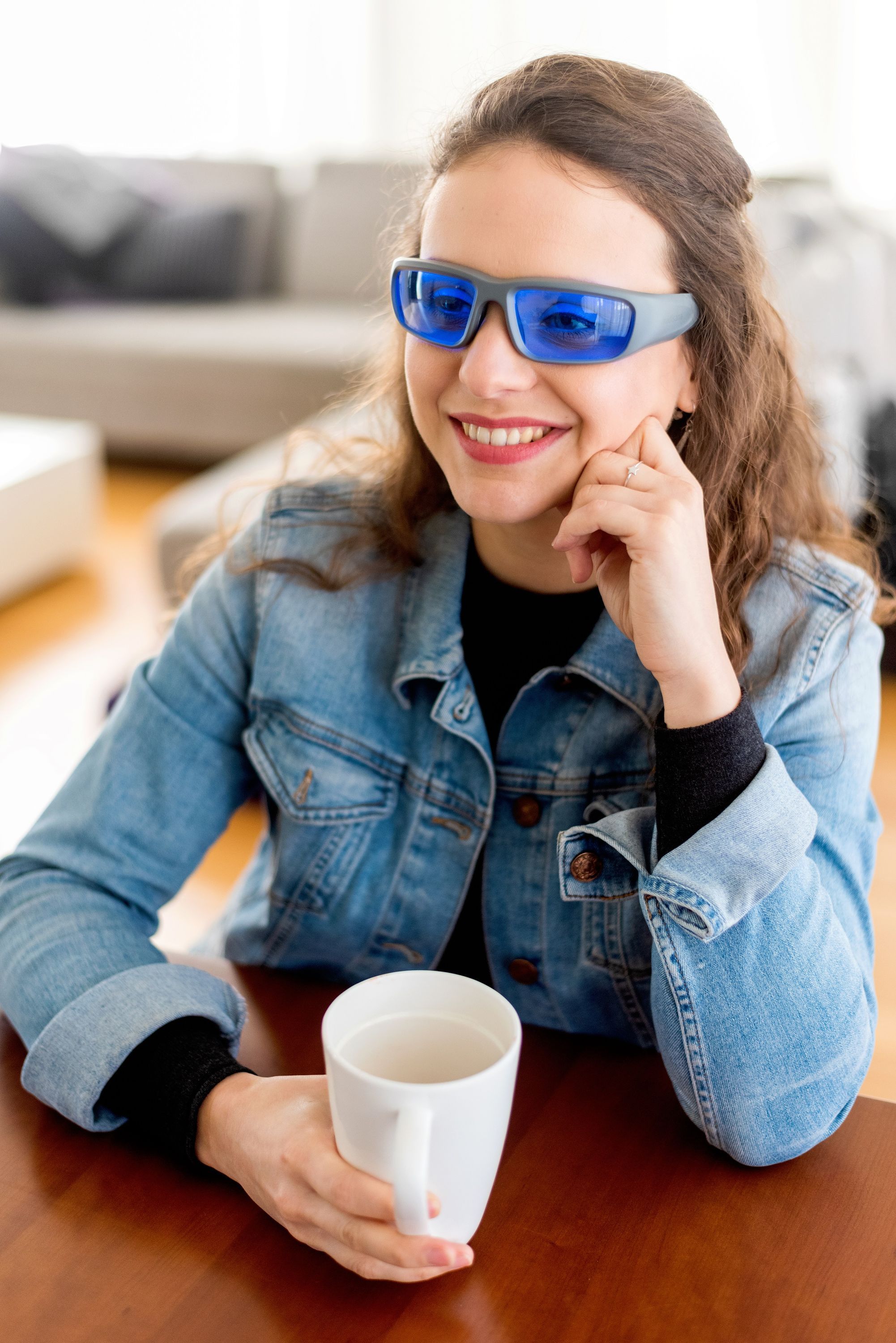 Frau mit Jeansjacke und Tageslichtbrille hält eine Tasse.