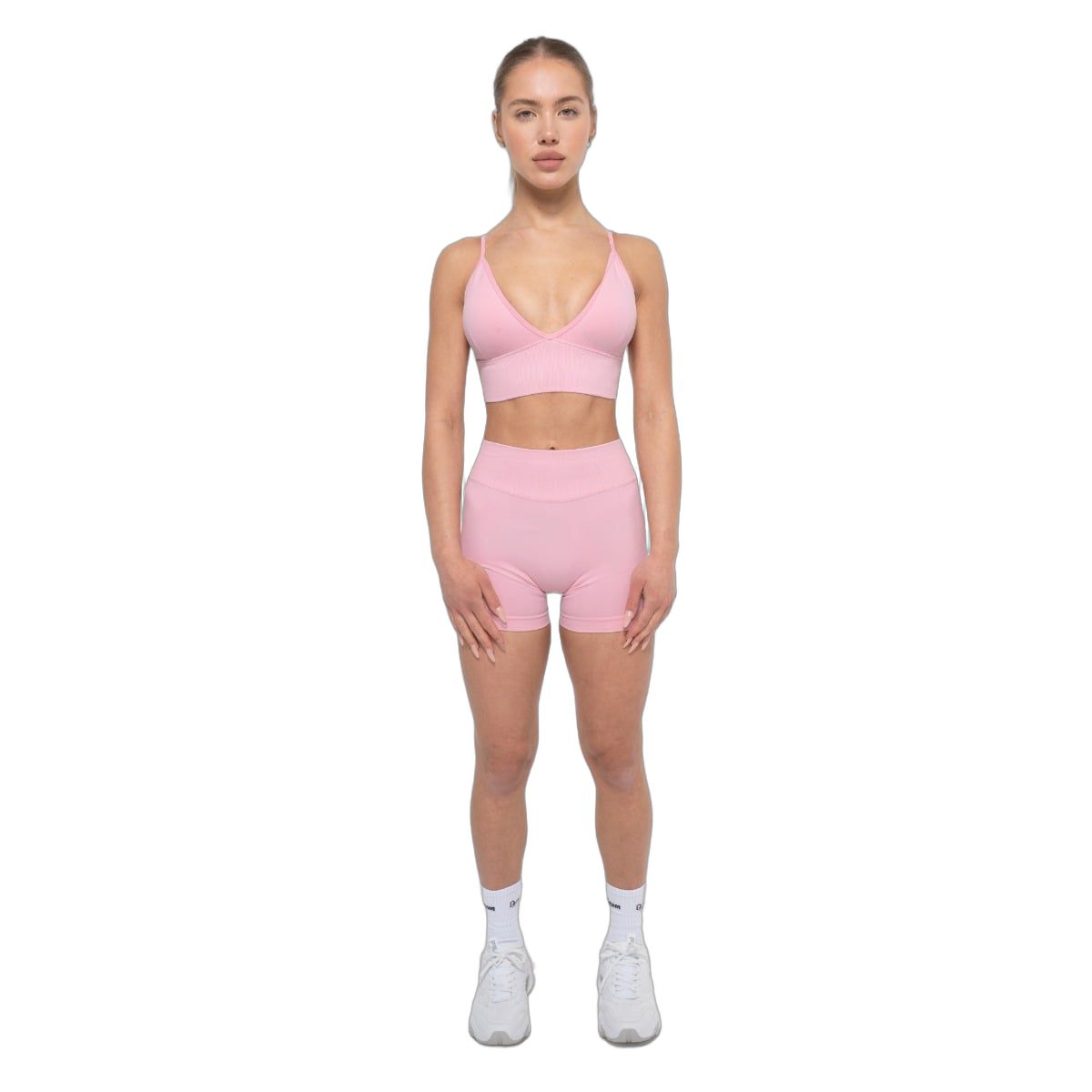 Frau in Baby Pink Sport-BH und Shorts. Steht frontal, weiße Socken und Schuhe.