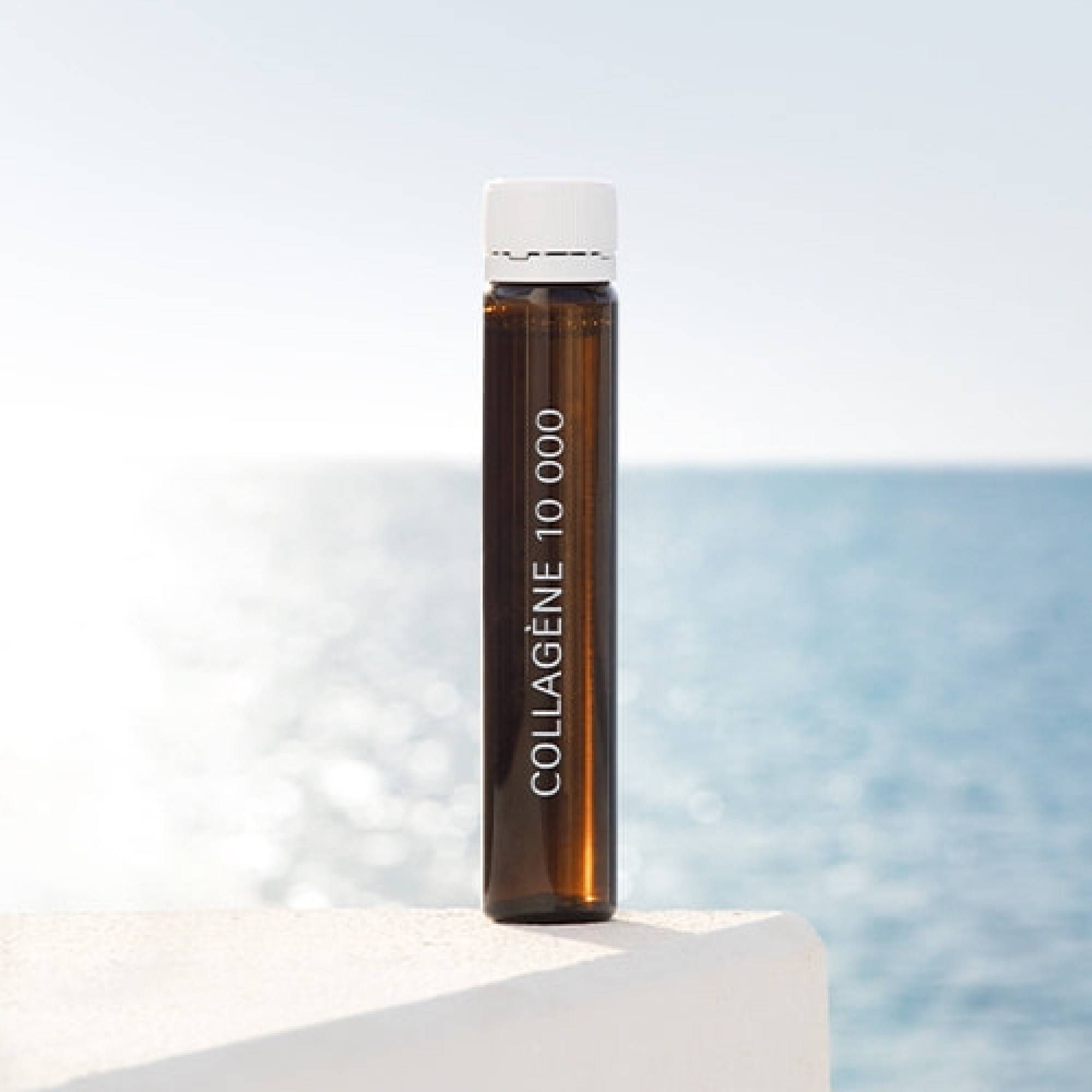 Braune Glasampulle mit weißem Verschluss. Vertikaler Schriftzug Collagène 10 000, vor Meerblick.