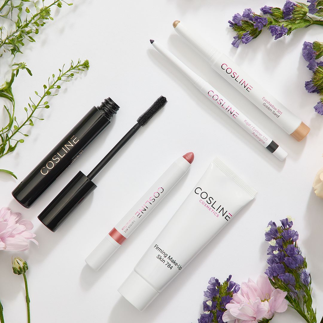 Kosmetikprodukte auf weißem Hintergrund mit Blumen. Enthalten: Mascara, Lidschattenstift, Kajalstift, Lippenstift und Tube.