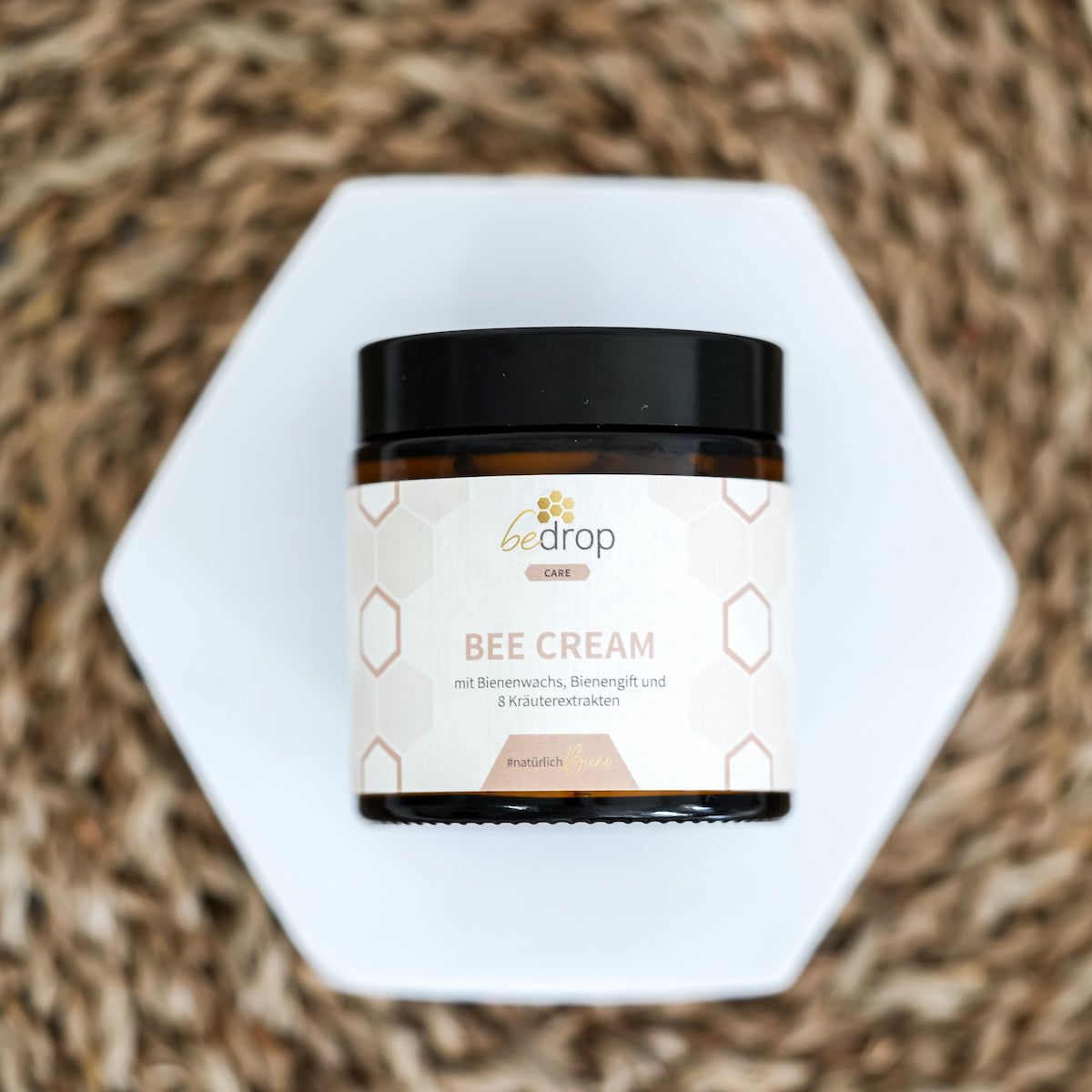 Braune Glasdose "bedrop Bee Cream" auf weißem Sechseck. Hintergrund mit Wabenmuster.