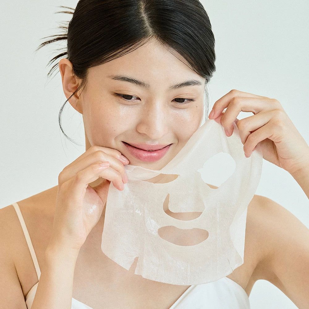 Frau hält Gesichtsmaske. Maske mit Aussparungen für Augen, Nase und Mund. Frau lächelt.