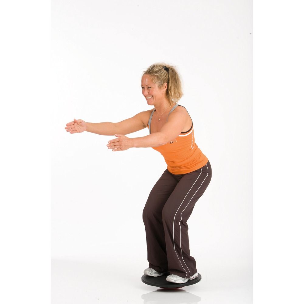 Frau steht auf einem Balance Board. Sie trägt Sportkleidung und balanciert mit ausgestreckten Armen.