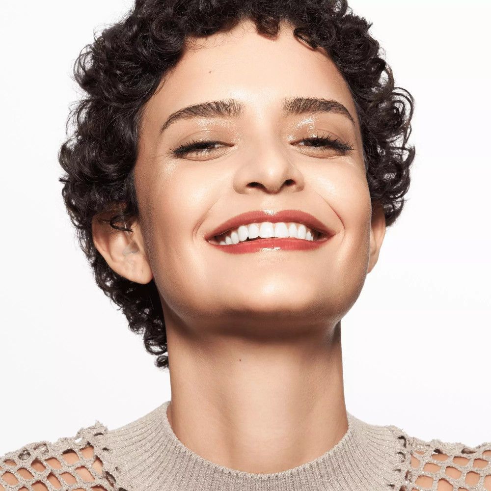 Frau mit lockigem Haar und Lippenstift. Sie lächelt. Lippen glänzend.