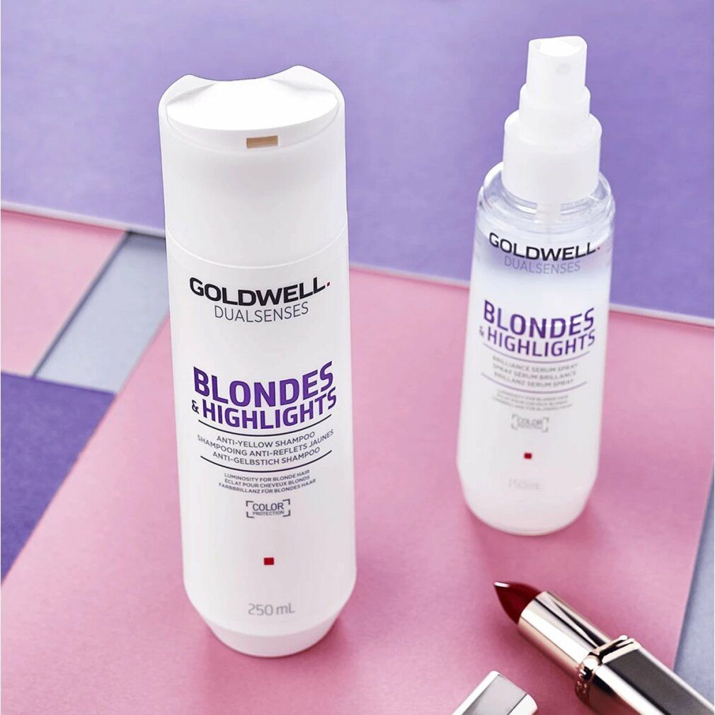 Zwei weiße Flaschen Goldwell Blondes & Highlights Shampoo. Eine mit Sprühkopf. Auf rosa und lila Hintergrund. Lippenstift.