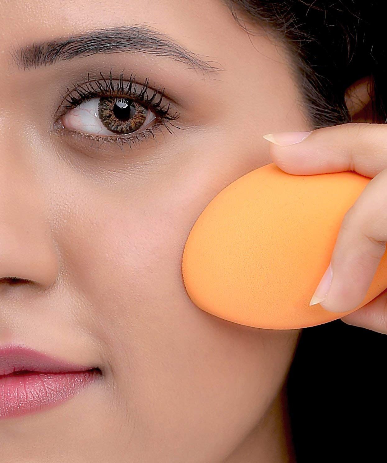 Orangefarbener Make-up-Schwamm, oval geformt, wird von einer Hand gehalten.