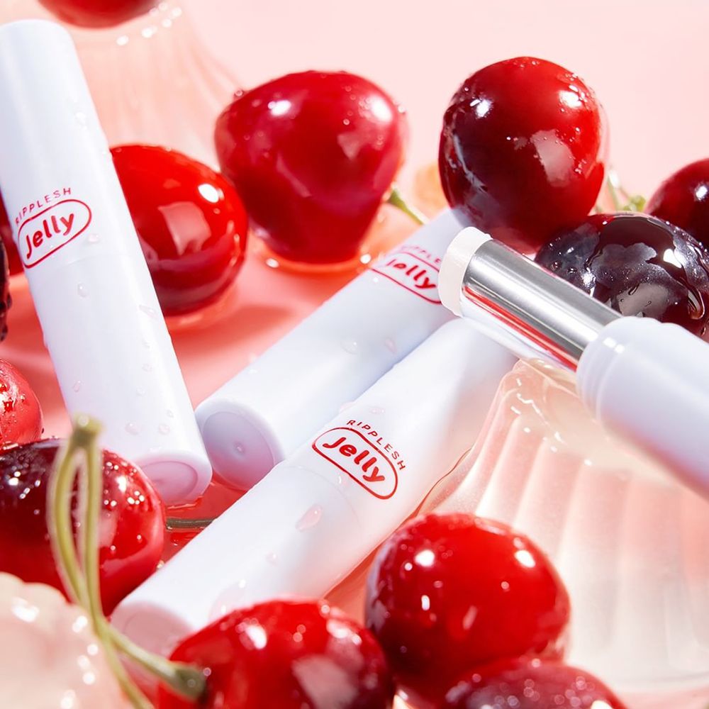 Weiße Lippenbalsam-Hülsen mit rotem "Jelly"-Logo, umgeben von Kirschen. Einige sind geöffnet.