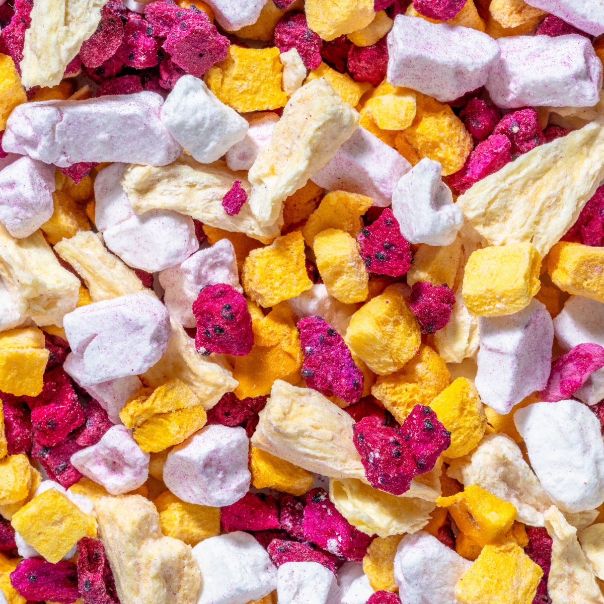 Nahaufnahme von gefriergetrockneten Früchten: gelbe, rosa und weiße Stücke. Verschiedene Formen und Größen.