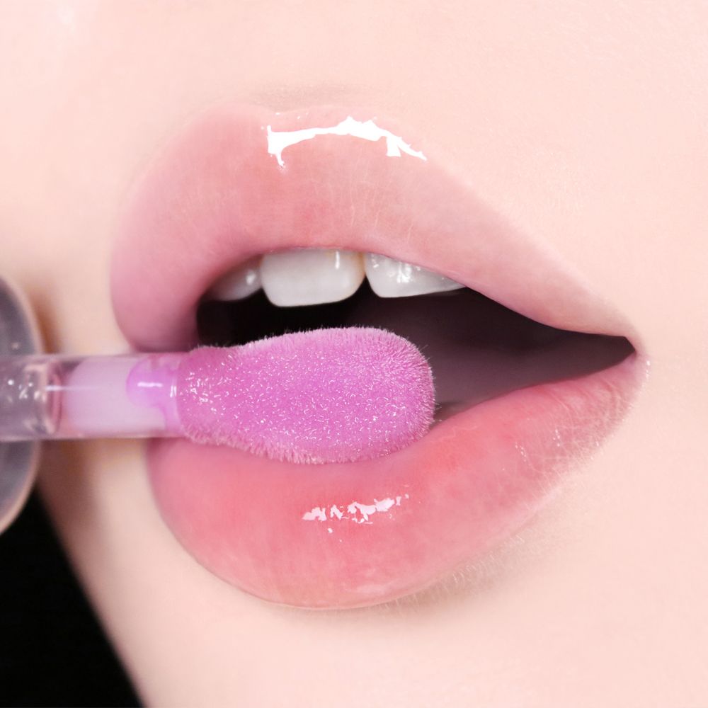 Nahaufnahme von Lippen, die mit einem Applikator mit lila Lip Oil benetzt werden. Glänzendes Finish.