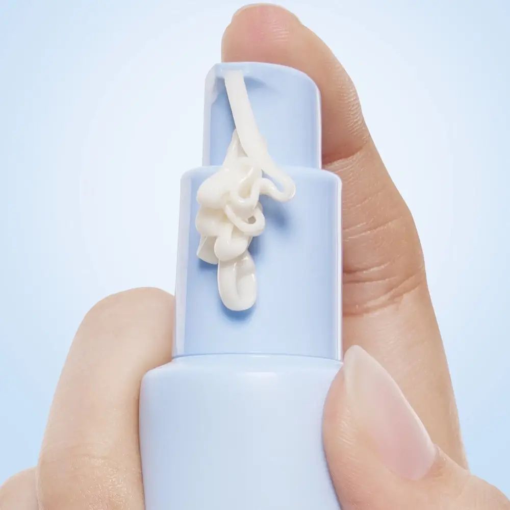 Nahaufnahme einer Hand, die eine hellblaue Tube hält. Creme wird aus der Öffnung gedrückt. Produktname nicht sichtbar.