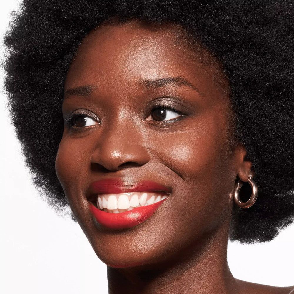 Porträt einer Frau mit dunkler Haut. Sie trägt roten Lippenstift und goldene Creolen.