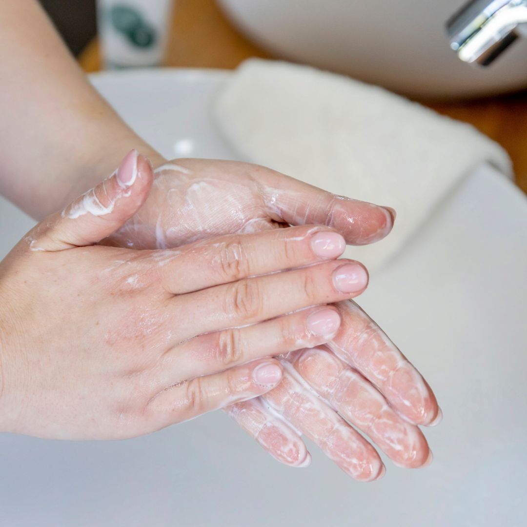 Hände mit Waschgel eingerieben. Waschbecken und Handtuch im Hintergrund.