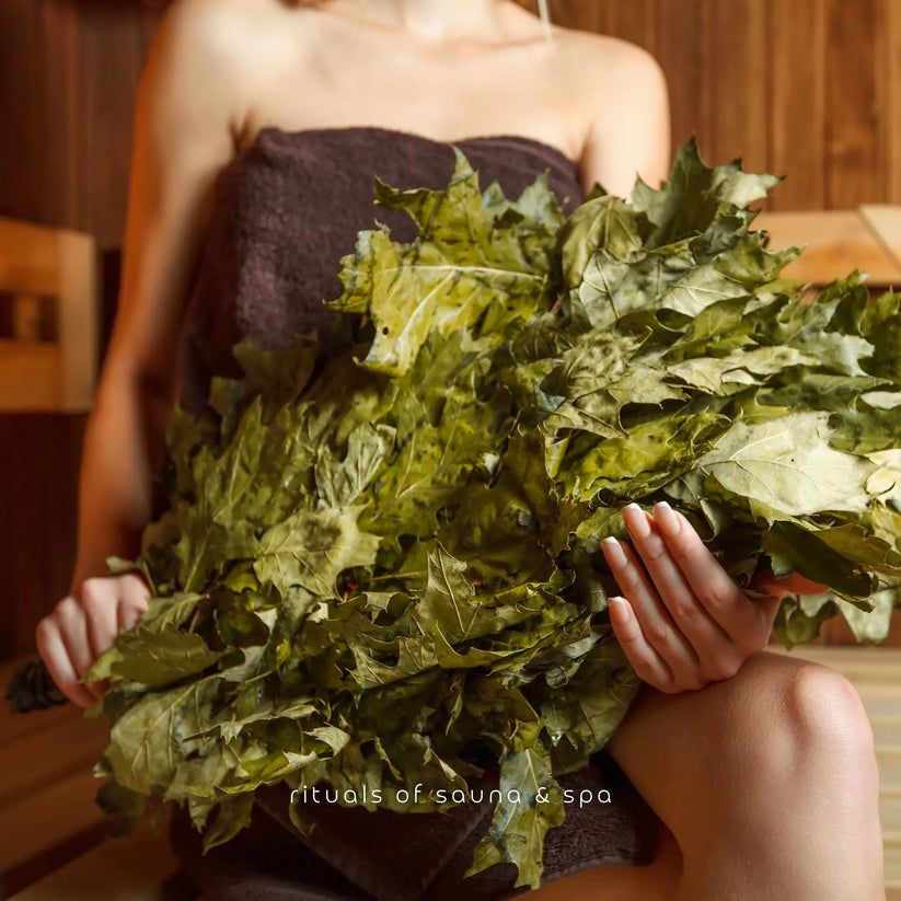 Person hält ein Bündel Blätter. Der Hintergrund zeigt eine Sauna.