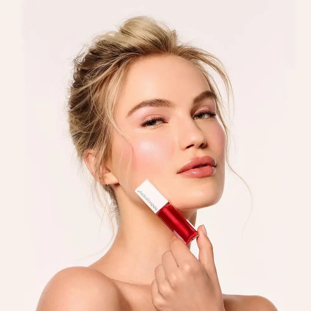 Frau hält Lipgloss. Der Deckel ist weiß, der Inhalt rot. Auf dem Deckel steht Bodyography.