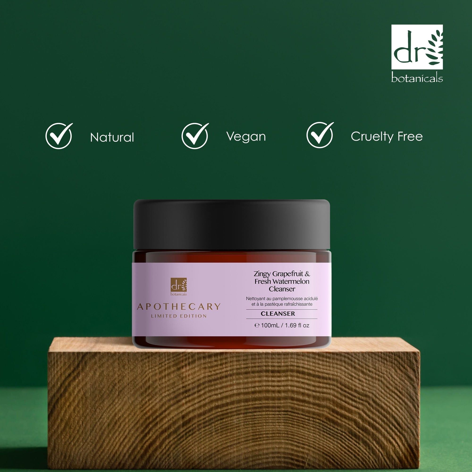 Braunes Glas mit schwarzem Deckel. Etikett mit Produktnamen und Marke. Aufschrift: Natural, Vegan, Cruelty Free. Auf Holzblock.