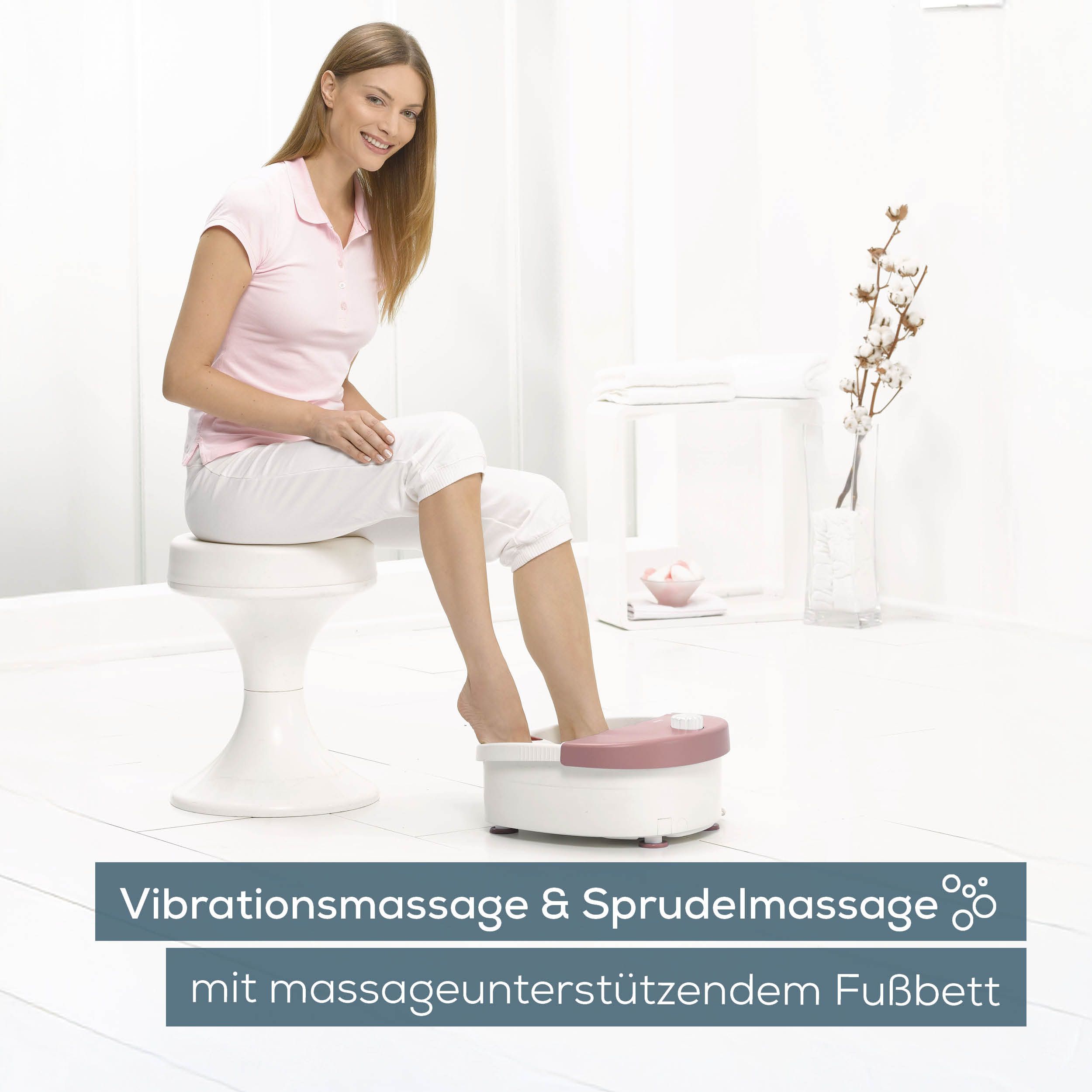 Fußsprudelbad mit Frau. Rosa-weißes Gerät, Frau sitzt auf Hocker. Text: Vibrationsmassage & Sprudelmassage.