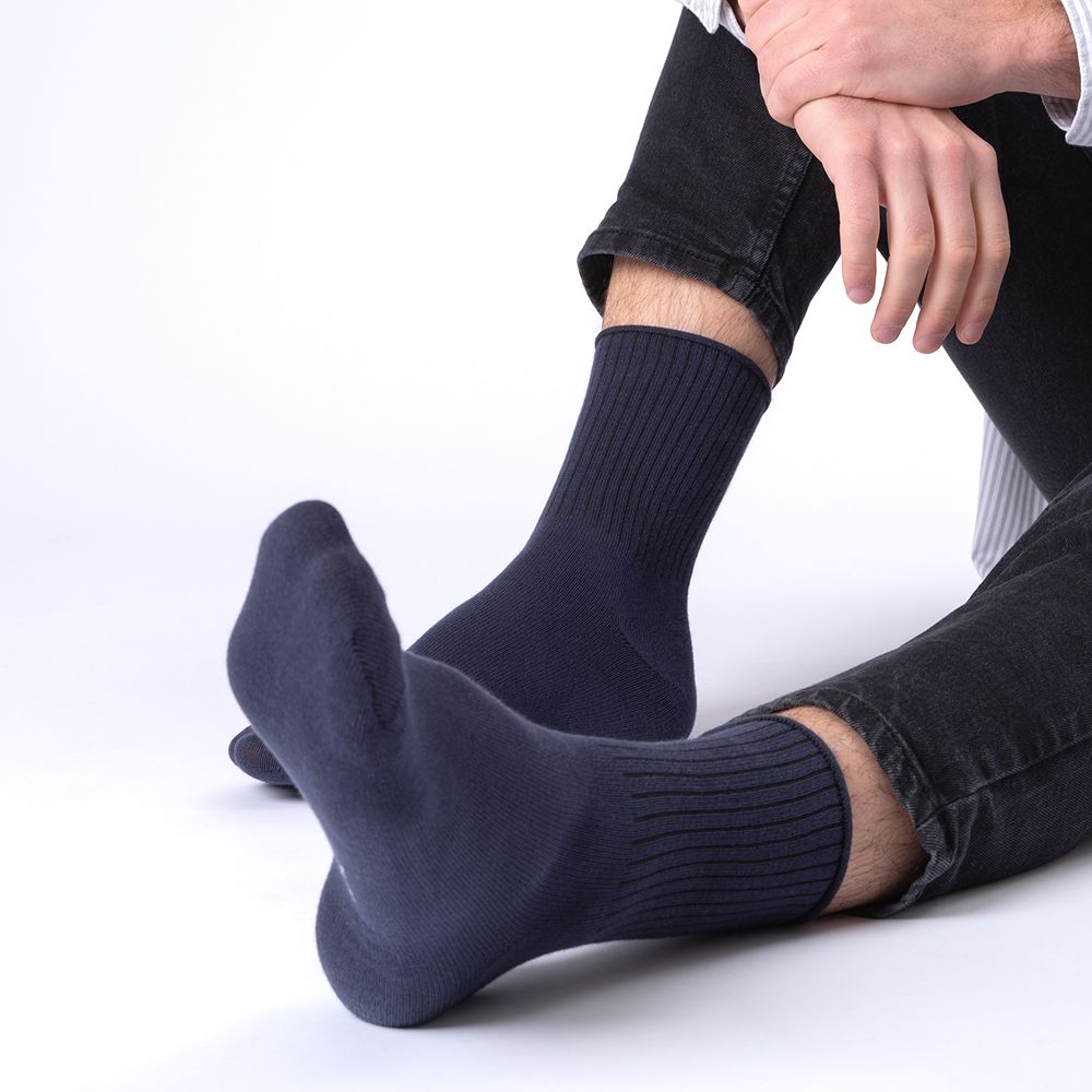 Marineblaue Socke am Fuß einer Person. Rippstrickbündchen. Person sitzt. Schwarze Hose.