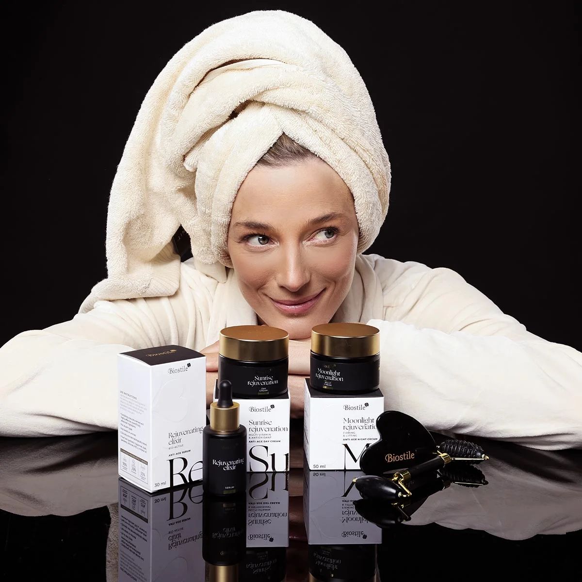 Frau mit Handtuch und Bademantel. Produkte des Anti-Age-Geschenksets auf dem Tisch. Gesichtspflegeprodukte und Roller.