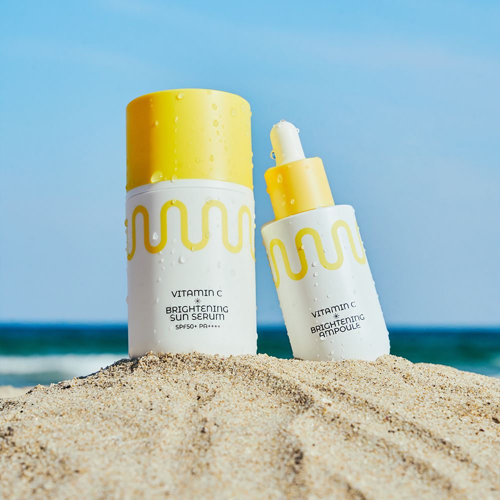 Weiße Flasche mit gelbem Verschluss und Wellenmuster, daneben eine Pipettenflasche. Am Strand.