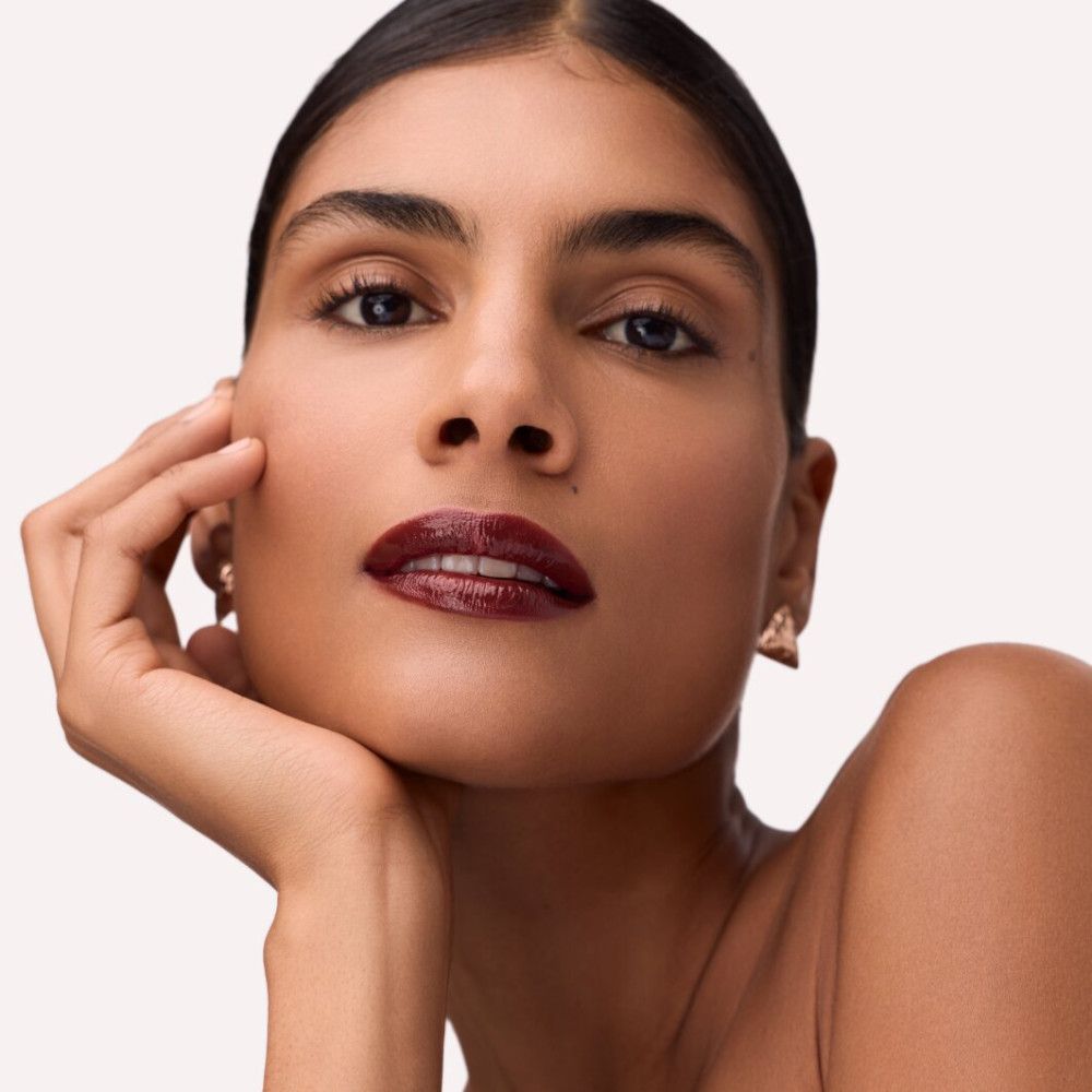 Porträt einer Frau mit tiefrotem Lip Tint auf den Lippen. Sie stützt das Kinn auf die Hand.