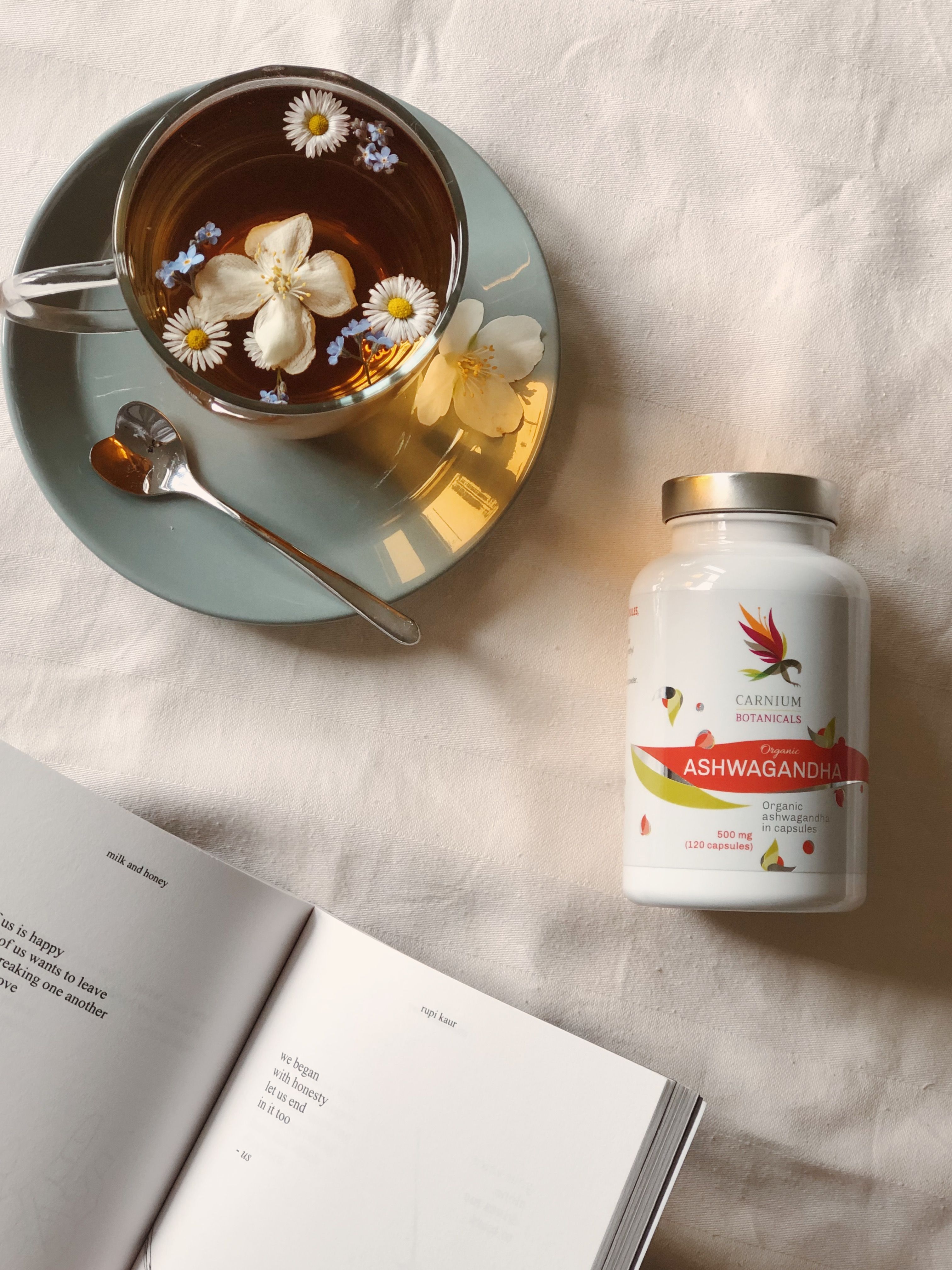 Flasche mit Kapseln neben einer Tasse Tee und einem offenen Buch. Etikett mit Produktname und Logo.